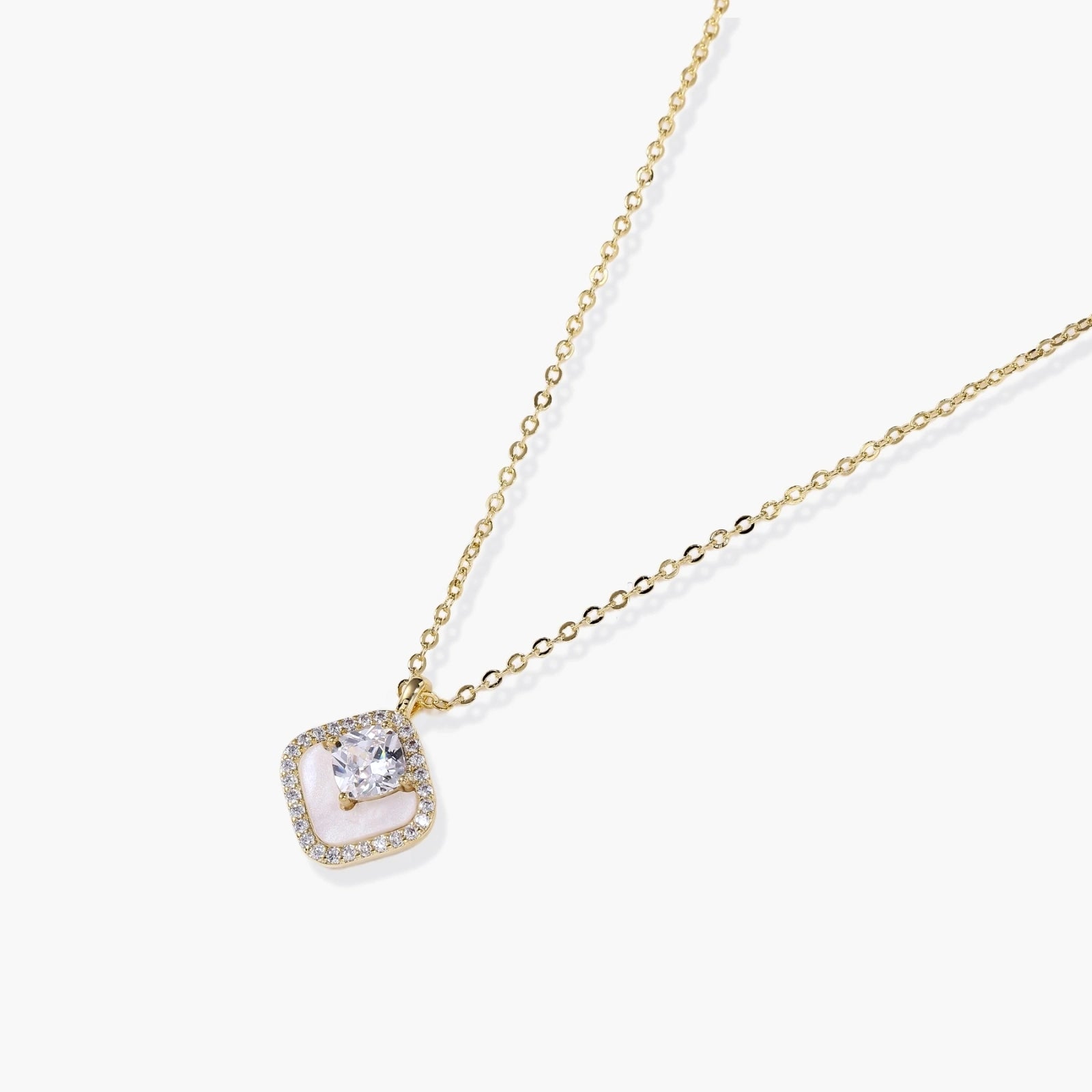 Gold quatrefoil pendant with crystal center on iridescent mother-of-pearl base, adjustable gold chain on cream background