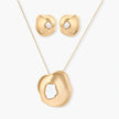 Close-up of organic gold-toned earrings and necklace with white baroque pearls on neutral background.
