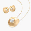 Close-up of organic gold-toned earrings and necklace with white baroque pearls on neutral background.