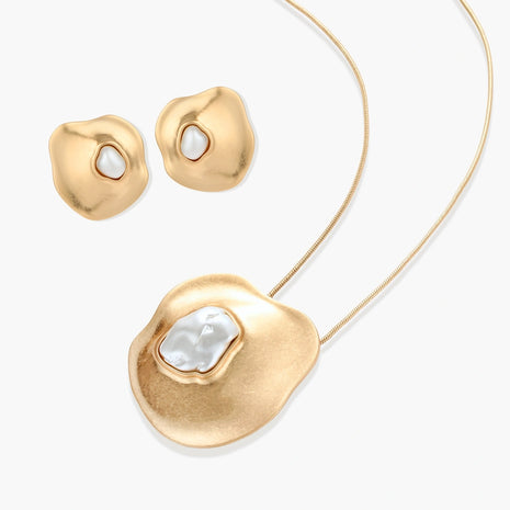 Close-up of organic gold-toned earrings and necklace with white baroque pearls on neutral background.