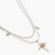 Layered silver-toned necklace set with cross pendant and gold sun charm detail, matching drop earrings on white background.