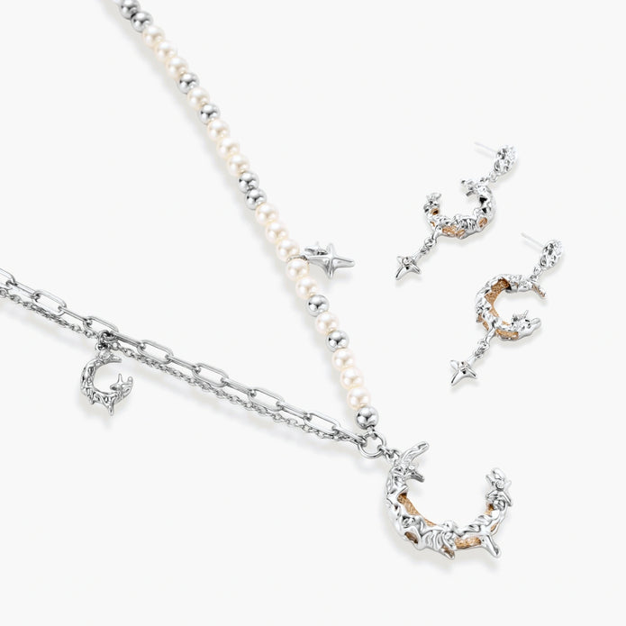 Mixed-metal jewelry set featuring layered necklaces with crescent moon pendant and pearl beads, plus matching star-drop earrings.