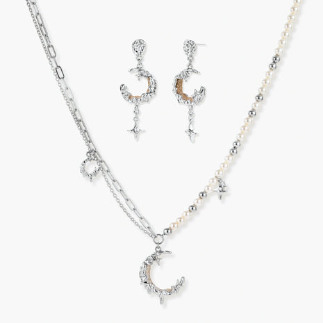 Mixed-metal jewelry set featuring layered necklaces with crescent moon pendant and pearl beads, plus matching star-drop earrings.