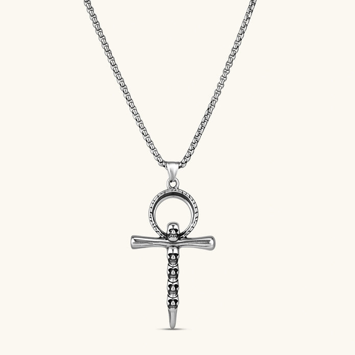 Silver stainless steel ankh pendant with skull motifs on vertical bar and textured ring top, on a box chain necklace.