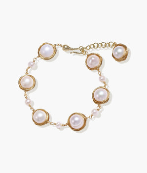 Gold wire-wrapped freshwater pearl bracelet with alternating pearl sizes on cream background, adjustable length