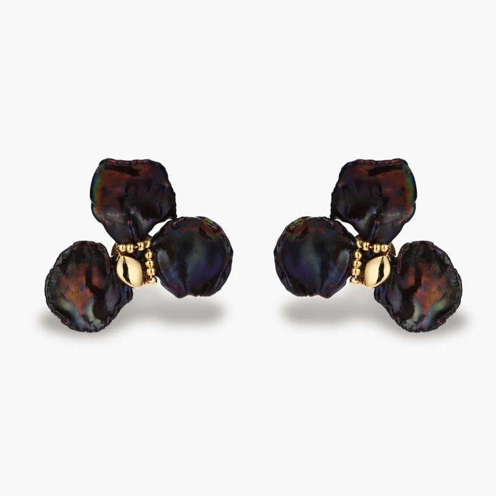 Dark iridescent baroque pearls arranged in flower pattern with 18K gold-plated center on cream background.
