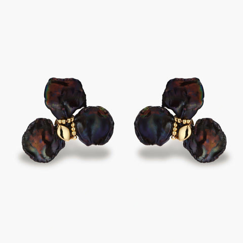 Dark iridescent baroque pearls arranged in flower pattern with 18K gold-plated center on cream background.