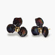Dark iridescent baroque pearls arranged in flower pattern with 18K gold-plated center on cream background.