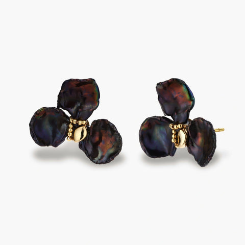 Dark iridescent baroque pearls arranged in flower pattern with 18K gold-plated center on cream background.
