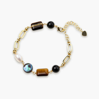 Gold chain bracelet with tiger's eye, obsidian, pearl, and iridescent abalone stones on cream background.